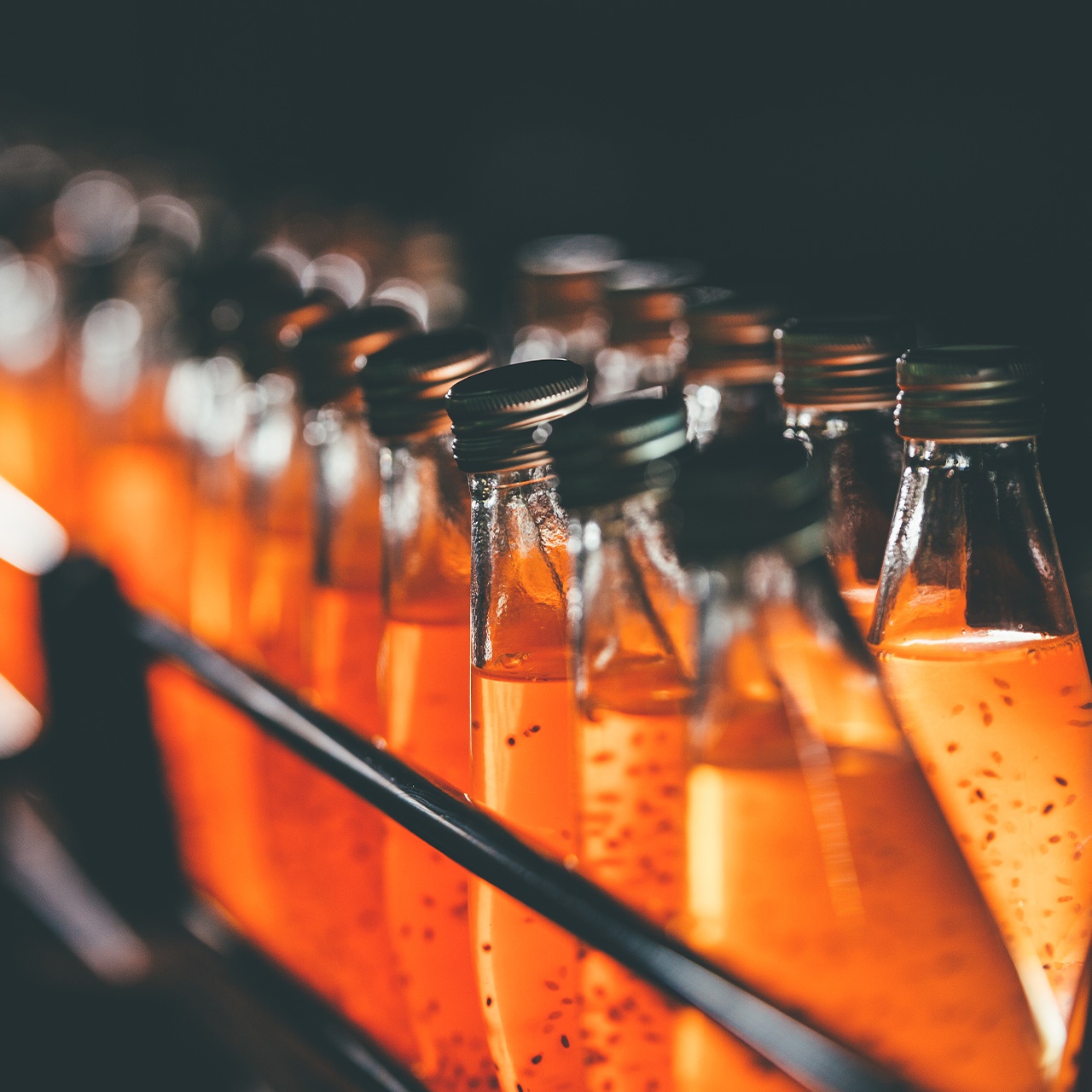 Glass bottles on a shelf with orange liquid and small pieces in them.